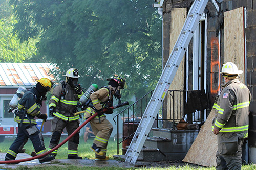 Three firefighters enter a burning building with a water hose