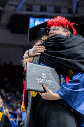 Eli hugging a mentor at graduation with his diploma in hand.