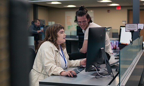 A coach works with a student in a computer lab