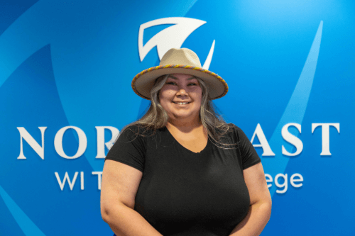 Individual wearing a hat smiling in front of a Northeast Wisconsin Technical College backdrop.