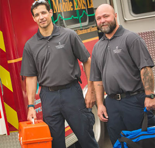 EMT instructors hold gear in front of ambulance