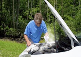 A man looks at the engine in his car while it is smoking