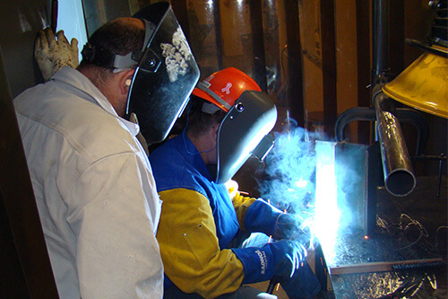 A worker welds while an instructor observes their work